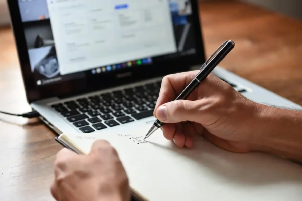 Person writing career growth action steps in a notebook next to a laptop displaying skill-building resources