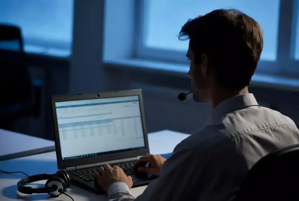 Customer support worker viewing data on a laptop screen in a dim office
