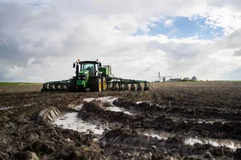 Large green corn planter working a muddy Iowa field under cloudy May skies