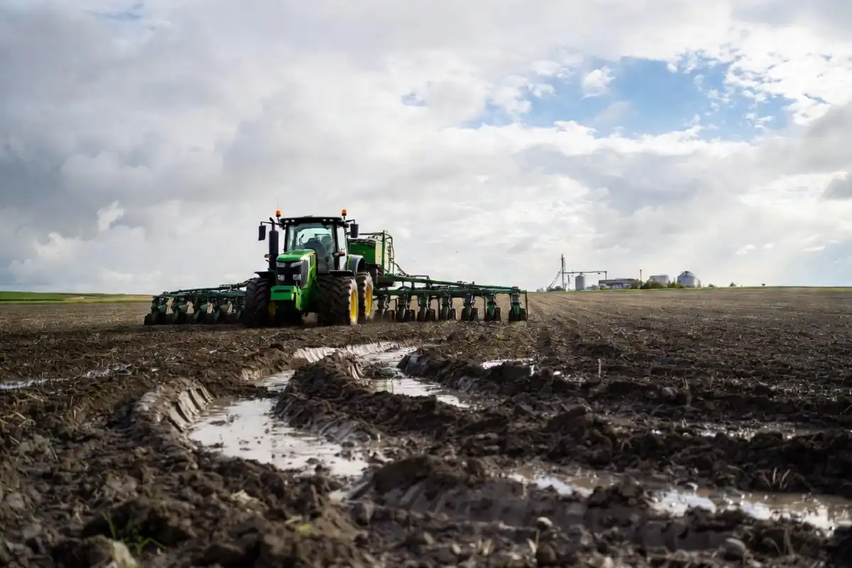 Large green corn planter working a muddy Iowa field under cloudy May skies