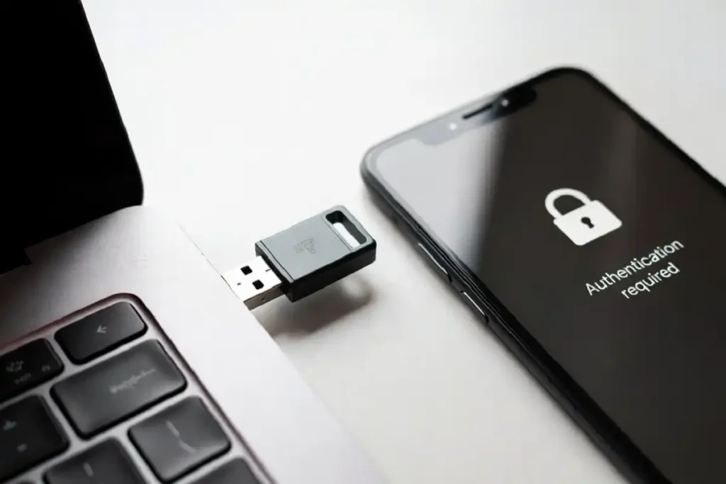 Hardware security key plugged into a laptop next to a smartphone