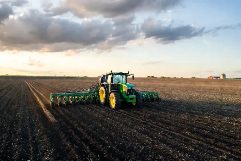 Green tractor pulling a planter through an Iowa cornfield under partly cloudy skies in late May 2026