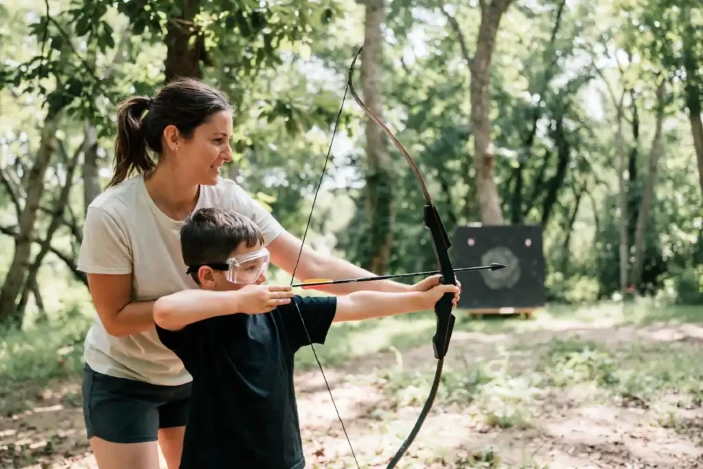 A DNR volunteer mentor teaching a young child archery at an outdoor recreation activity station