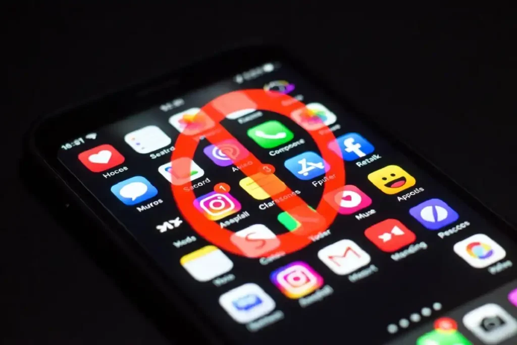 Social media app icons on a smartphone screen with a ban symbol representing Canada's new age restriction under the Safe Social Media Act
